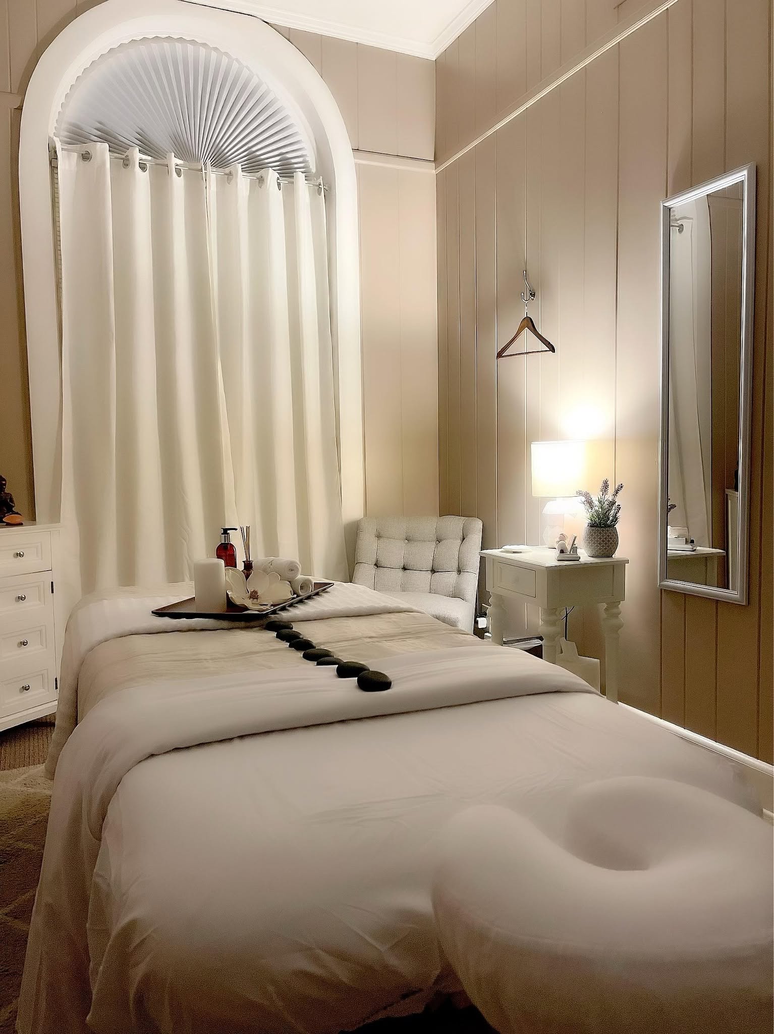 Marisol's candlelit treatment room, with warm cream linens, hot stones laid along the table, and an arched curtained window